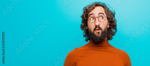 young bearded crazy man with a worried, confused, clueless expression, looking up to copy space, doubting against flat color wall