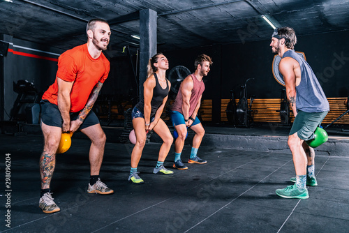 Muscular fellows with coach lifting up kettle bells while functional training in contemporary health club photo