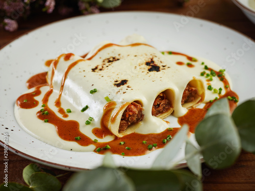 Closeup hake and txangurro cannelloni with oxtail served with bechamel sauce on ceramic plate