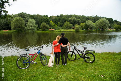 Влюбленная пара с собакой в парке у пруда после велопрогулки