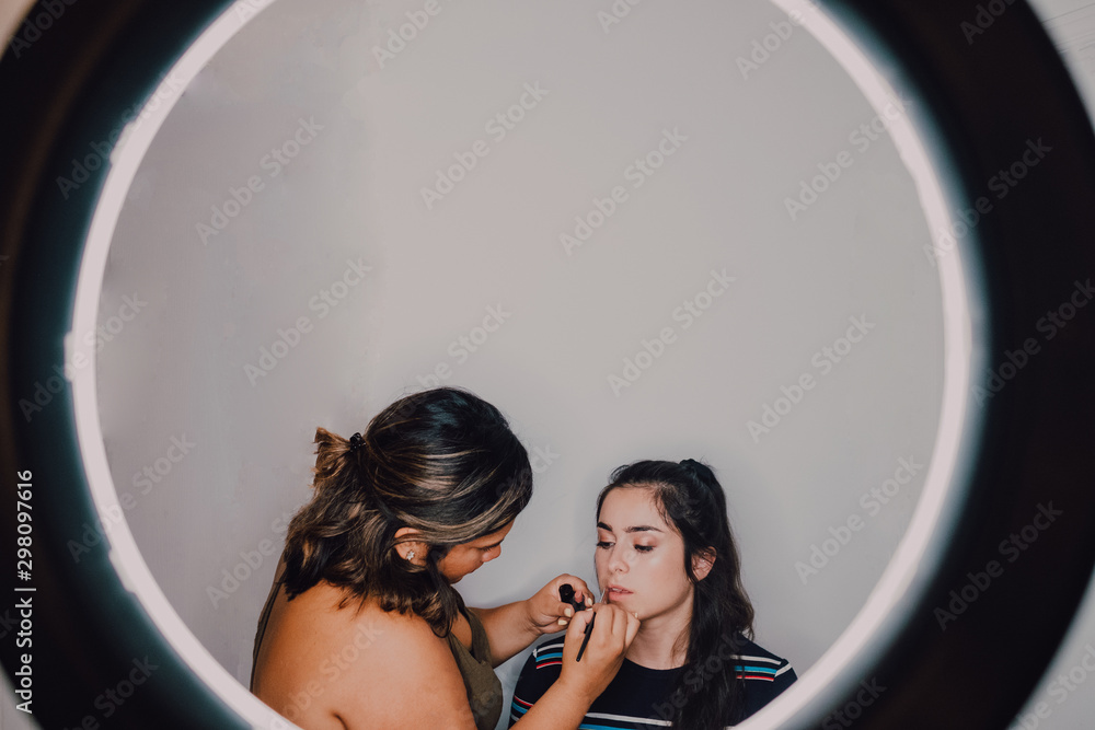 Young professional makeup artist putting lipstick on young clients lips in studio through a light ring Young professional makeup artist putting lipstick on young clients lips in studio through a light ring