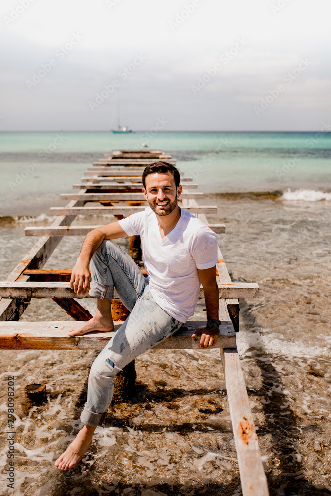 Laughing man in casual wear resting on aged pier in summer and looking at camera Laughing man in casual wear resting on aged pier in summer and looking at camera