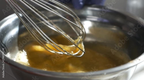 Girl whips the raw eggs with sugar in a glass bowl. Whisking the eggs