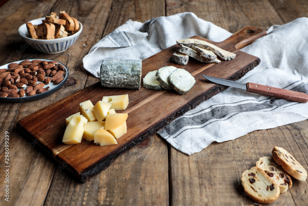 Sweet croutons with raisins and plate with almonds placed on wooden table near board with various cut cheese Sweet croutons with raisins and plate with almonds placed on wooden table near board with various cut cheese