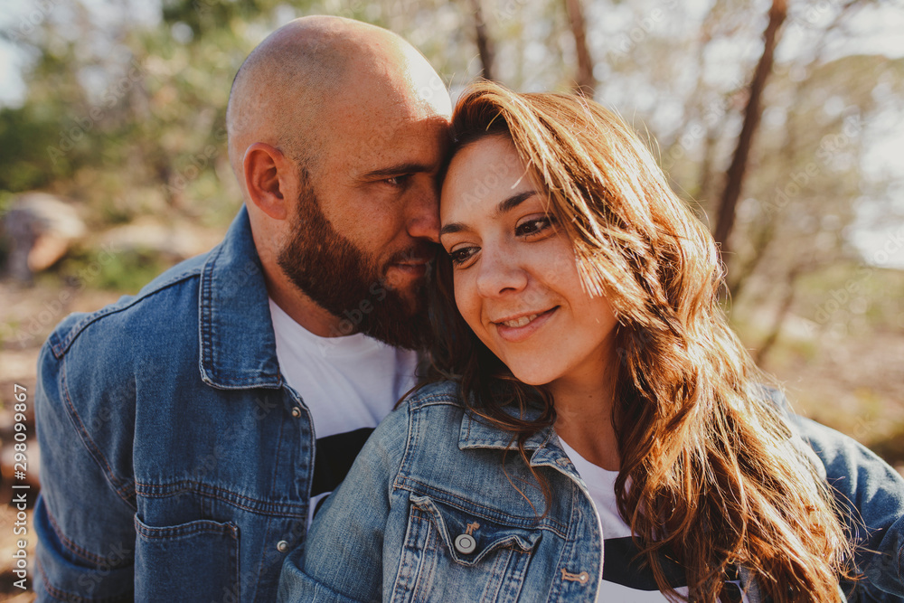 Happy loving couple in denim jackets cuddling while sitting close in countryside on sunny day Happy loving couple in denim jackets cuddling while sitting close in countryside on sunny day