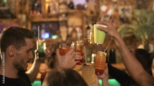 Handheld shot of group of cheerful young people of different ethnicities holding glasses with cocktails while dancing at party at bar or nightclub photo