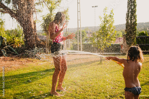 Excited teen girl laughing and playing with jet of clean water while having fun in garden on sunny day