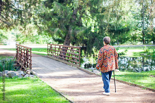 Rear view of senior woman walking with cane in park. Granny standing at bridge outdoors. Retirement concept