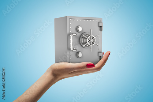 Canvas-taulu Close-up of woman's hand facing up and holding small grey money safe on light-blue background