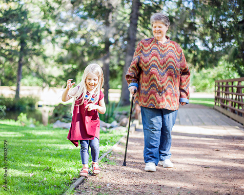 Happy little girl laughing in park, grandmother looking at her. Kid walking together with granny in summer