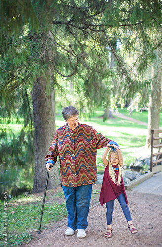 Happy little girl and her granny having fun together in park. Funny kid holding hand of grandmother in forest