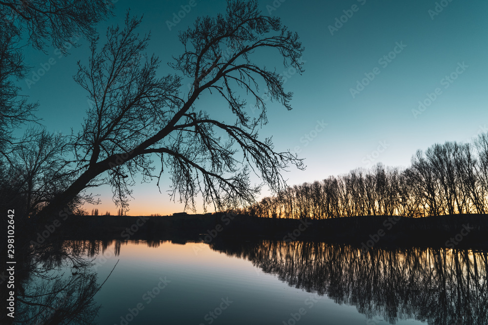 Landscape of silhouettes of trees and reflection in the river at sunset. Contrast cold and warm colors in autumn. Romantic sunset Landscape of silhouettes of trees and reflection in the river at sunset. Contrast cold and warm colors in autumn. Romantic sunset
