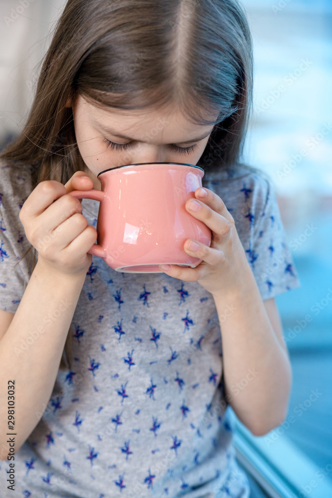 Closeup portrait of a cute little girl with a white milk mustache, pleased charming child with a smile holds a glass, drinks milk before bedtime