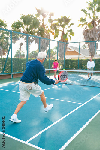 Group of active seniors, men and women, playing platform tennis on tennis court.