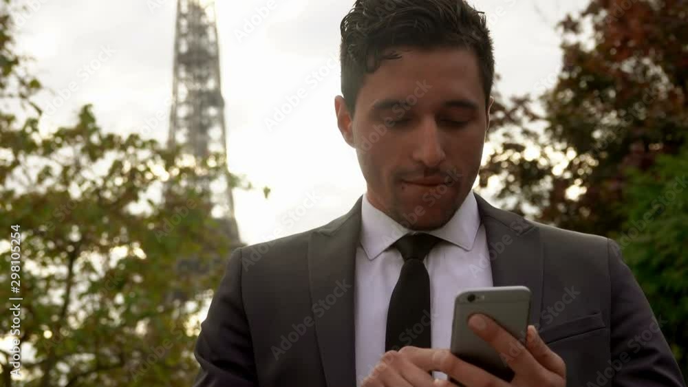 Young attractive businessman in a black suit sends a message on a cell phone on the background of the Eiffel Tower Young attractive businessman in a black suit sends a message on a cell phone on the background of the Eiffel Tower