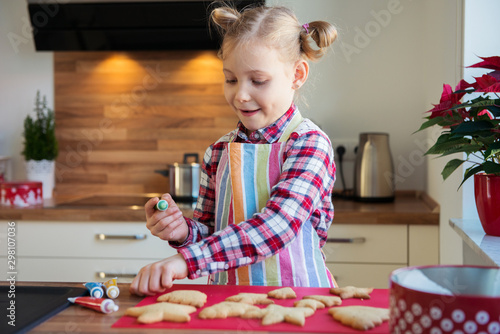 Pretty little girl with funny pigtails decoraiting christmas cookies of different forms in kitchen photo