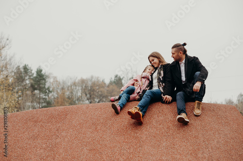 Happy family. The father and mother embracing their daughter relaxing outdoors in autumn park