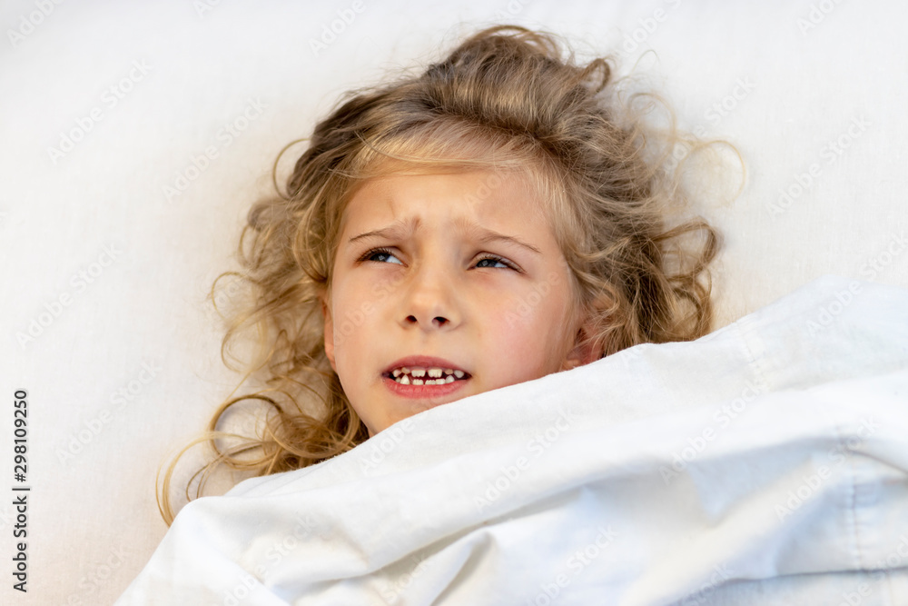 a girl with blond hair she lies in bed under a blanket. she is sad