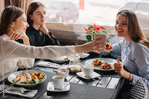 Three girlfriends having lunch together at cafe . One o them showing something on her phone for other one