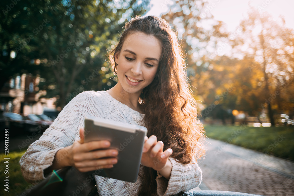 Joyful girl in autumn scenery using digital tablet outdoors browsing internet Joyful girl in autumn scenery using digital tablet outdoors browsing internet