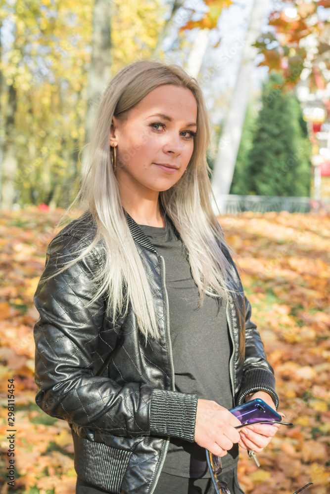 Beautiful young hipster girl in a black leather jacket is photographed in an autumn park on a background of yellow fallen foliage Beautiful young hipster girl in a black leather jacket is photographed in an autumn park on a background of yellow fallen foliage