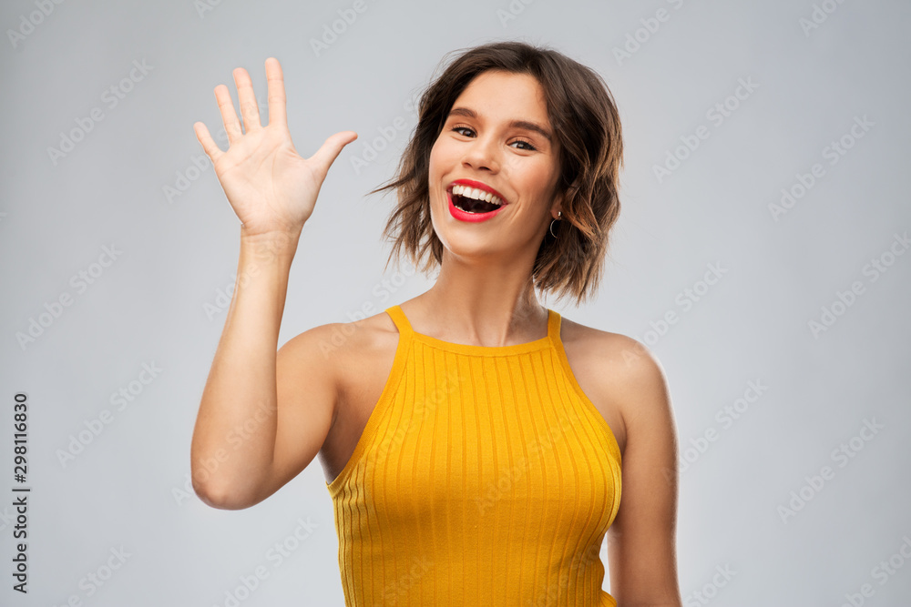 gesture, emotion and people concept - happy smiling young woman in mustard yellow top waving hand over grey background gesture, emotion and people concept - happy smiling young woman in mustard yellow top waving hand over grey background
