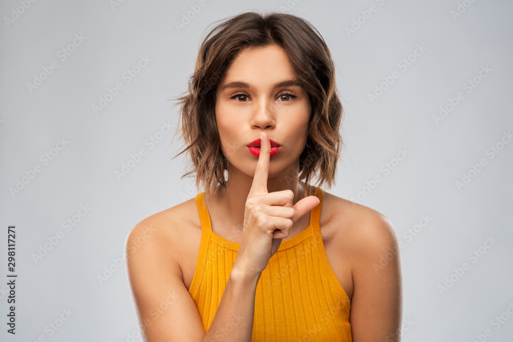 silence, secret, confidentiality concept - young woman in mustard yellow top making hush gesture over grey background silence, secret, confidentiality concept - young woman in mustard yellow top making hush gesture over grey background