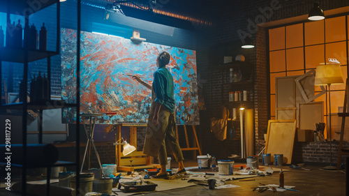 Talented Female Artist Works on Abstract Oil Painting, Using Paint Brush She Creates Modern Masterpiece. Dark and Messy Creative Studio where Large Canvas Stands on Easel Illuminated. photo