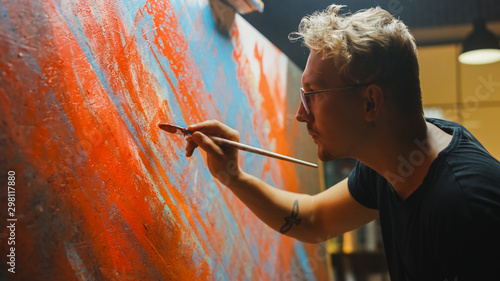 Portrait of Artist Working on Abstract Painting, Uses Paint Brush To Create Daringly Emotional Modern Picture. Dark Creative Studio Large Canvas Stands on Easel Illuminated. Side View Close-up Shot  photo