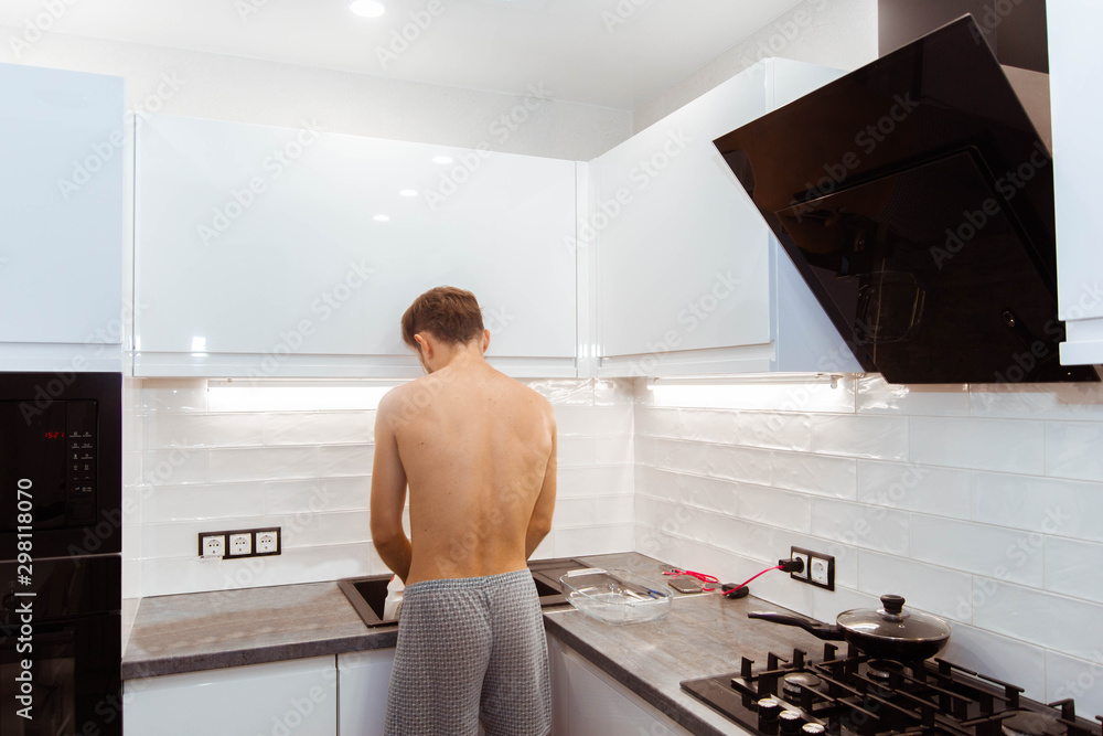 young man with a naked torso washes dishes in the kitchen. Male housekeeper. young man with a naked torso washes dishes in the kitchen. Male housekeeper.