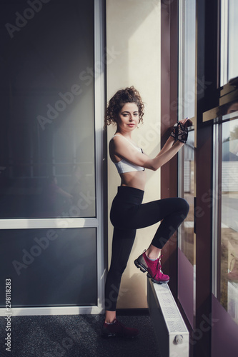 full length shot of a woman in leggings warming up before training in the gym