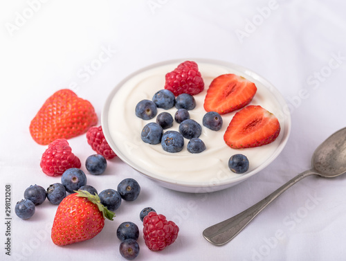 Yogurt in white bowl with strawberries and blueberries on white background.