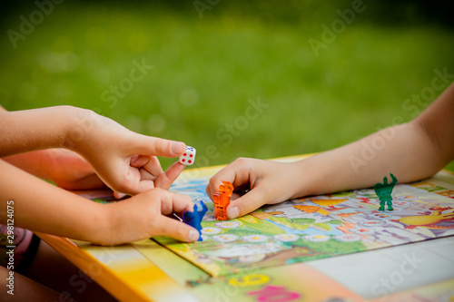 Family playing a board game, one kid is on the move and capturing the piece of another player.Games in Kindergarden.Board game and kids leisure concept. Kids holding red people figure in hand. blue