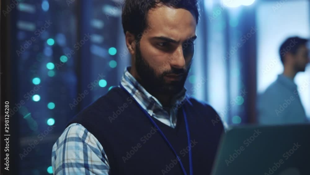 Server data IT specialist running diagnostics test on laptop with computer rack servers. Close-up. Team of administrators inspecting huge data center cyber security system.