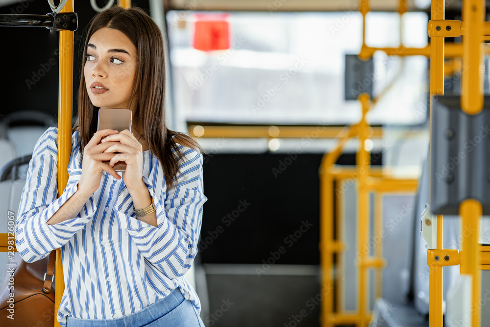 Smiling Woman Texting On Phone in Bus. Portrait Of Beautiful Happy Female In Stylish Casual Clothes texting with Mobile Phone While Riding In Public Transport. High Quality Image.