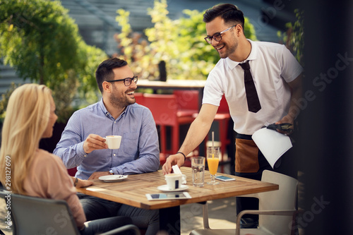 Happy waiter communicating with guests while setting their table for lunch.