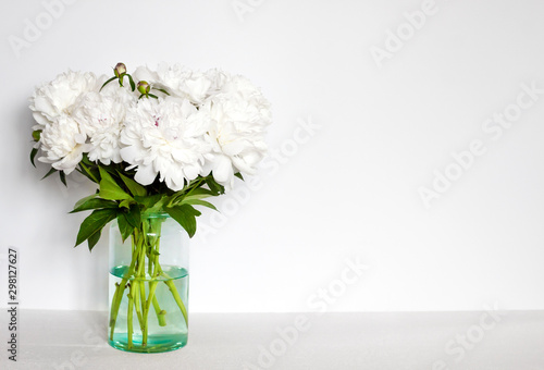 Bouquet of white peonies in a glass vase on a white wall background