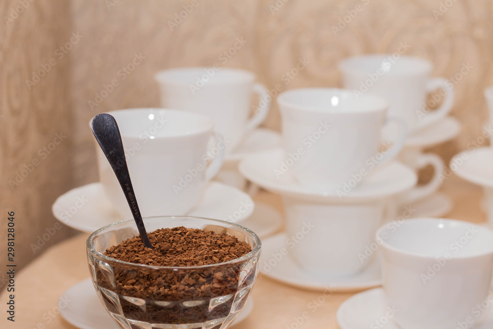Instant coffee in a glass bowl on a background of white coffee cups Instant coffee in a glass bowl on a background of white coffee cups