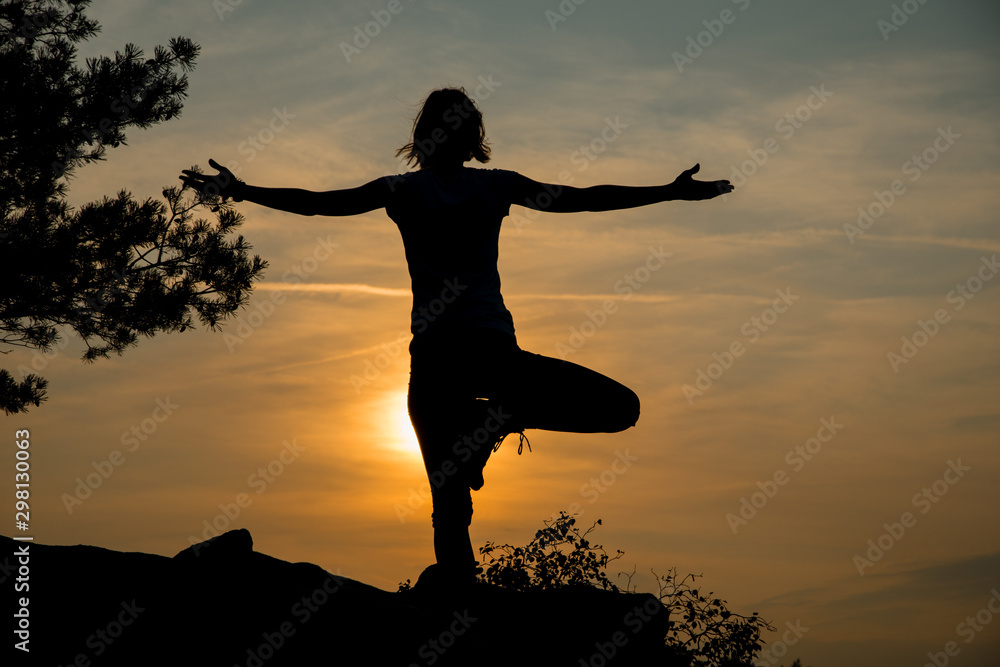 Young woman exercising yoga at dawn against sun, outdoor peace