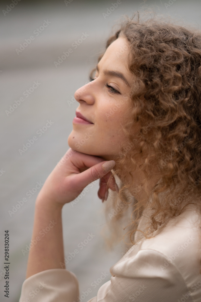 Φωτογραφία Profile view of young woman with curly hair resting her head on her hand