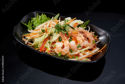 Salad with Beijing cabbage and shrimp on a black plate on a dark background
