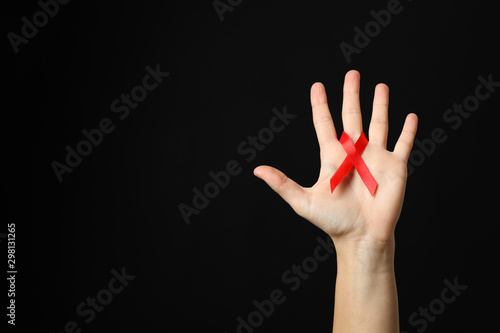 Hand and red awareness ribbon against black background, space for text