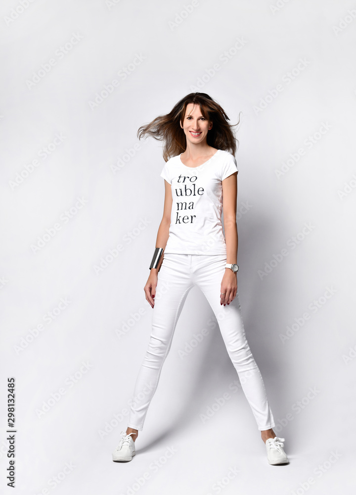 Smiling tall slender woman in white t-shirt, tight jeans and sneakers is  standing with her legs wide apart on white Photos | Adobe Stock