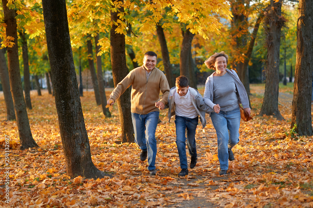 Happy family having holiday in autumn city park. Children and parents running, smiling, playing and having fun. Bright yellow trees and leaves Happy family having holiday in autumn city park. Children and parents running, smiling, playing and having fun. Bright yellow trees and leaves