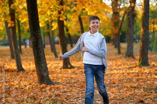 Boy teenager having holiday in autumn city park, running, smiling, playing and having fun. Bright yellow trees and leaves