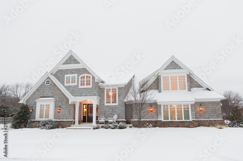 Wood shingled home in snow with warm lights illuminating windows