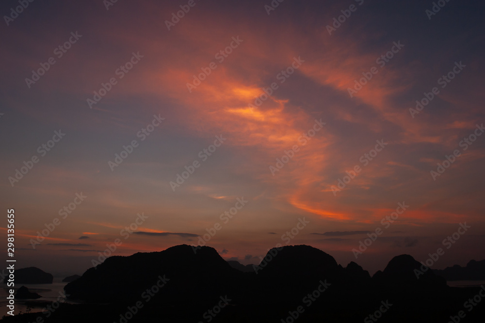 A picturesque sunset over the sea with a dark silhouette of the rocks. Dark cliffs with beautiful pink clouds and light on the sky. Red gleams from the sun in the evening sky.