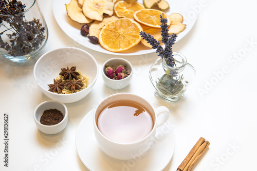 a white mug on a white table with herbal tea and herbal ingredients laid out on the table. Concept on the topic of herbal treatment for colds and flu in autumn