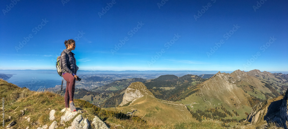 Young woman hiker with backpack on a mountain top against sky background, panoramic view. Travel concept