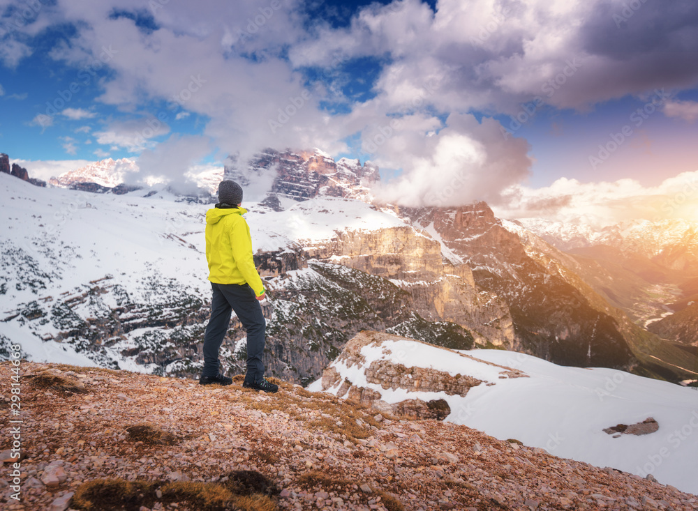 Young man in yellow jacket on the hill against snowy mountains at sunset in autumn. Landscape with sporty guy, rocks in snow, orange grass, blue sky with clouds. Travel in Italy in fall. Tourism Young man in yellow jacket on the hill against snowy mountains at sunset in autumn. Landscape with sporty guy, rocks in snow, orange grass, blue sky with clouds. Travel in Italy in fall. Tourism